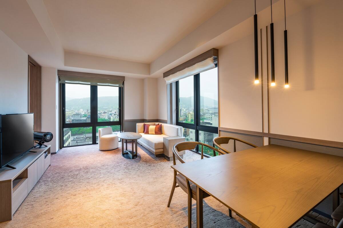 Una sala de estar moderna con un ventanal grande, un televisor de pantalla plana, una mesa de comedor y un sofá.