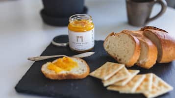 Una tabla de pizarra negra con un tarro de mermelada de naranja, un cuchillo, y rebanadas de pan y galletas.