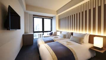 A hotel room with two beds, a TV mounted on the wall, a window with a view of the city, and a bedside table with a lamp.
