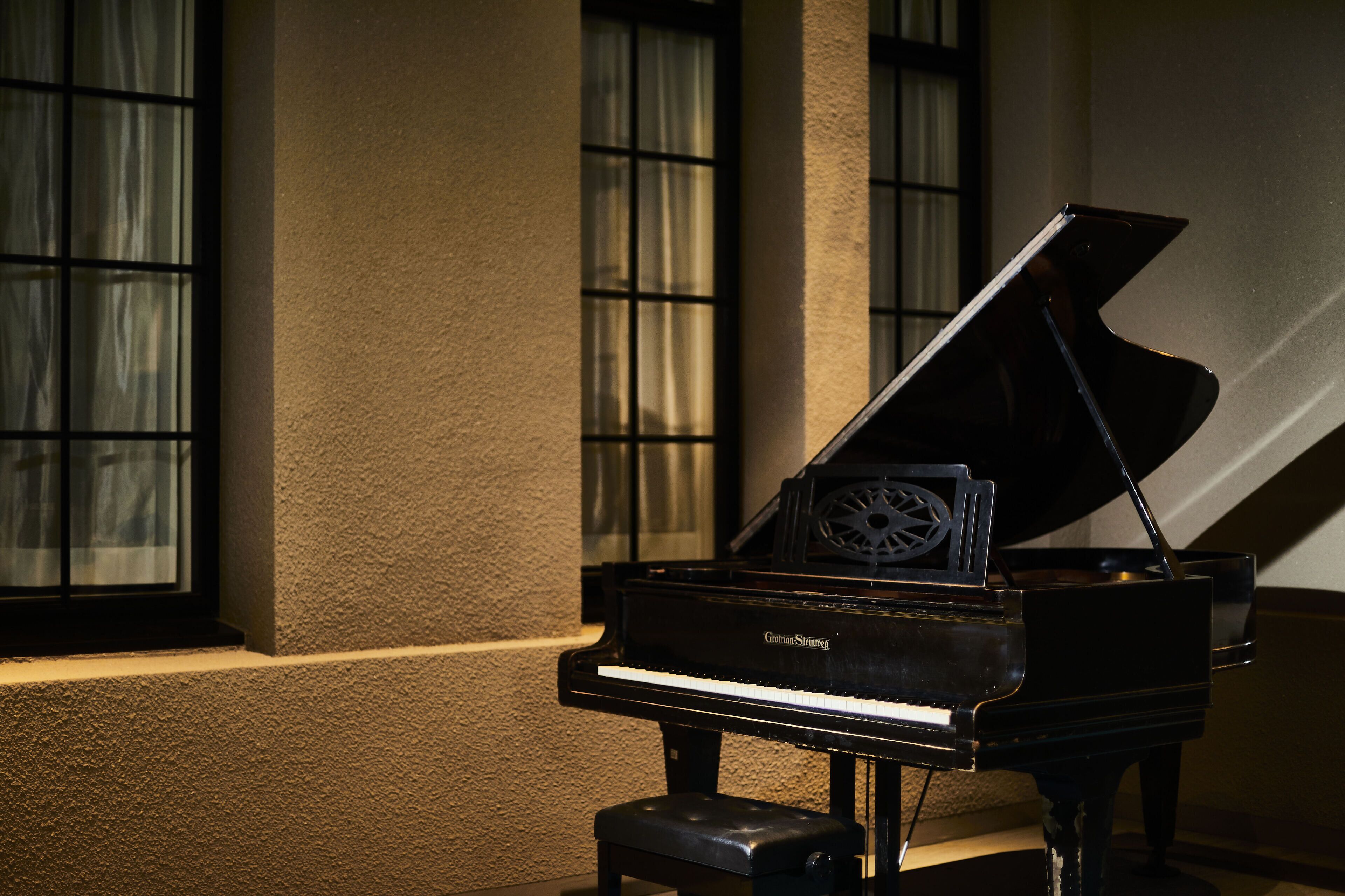 A grand piano in a room with large windows and a textured wall.