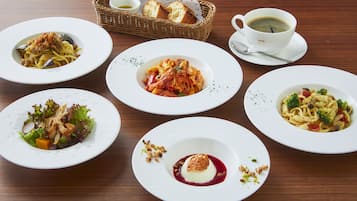 Una mesa con cinco platos de pasta, un cesto de pan y una taza de café.