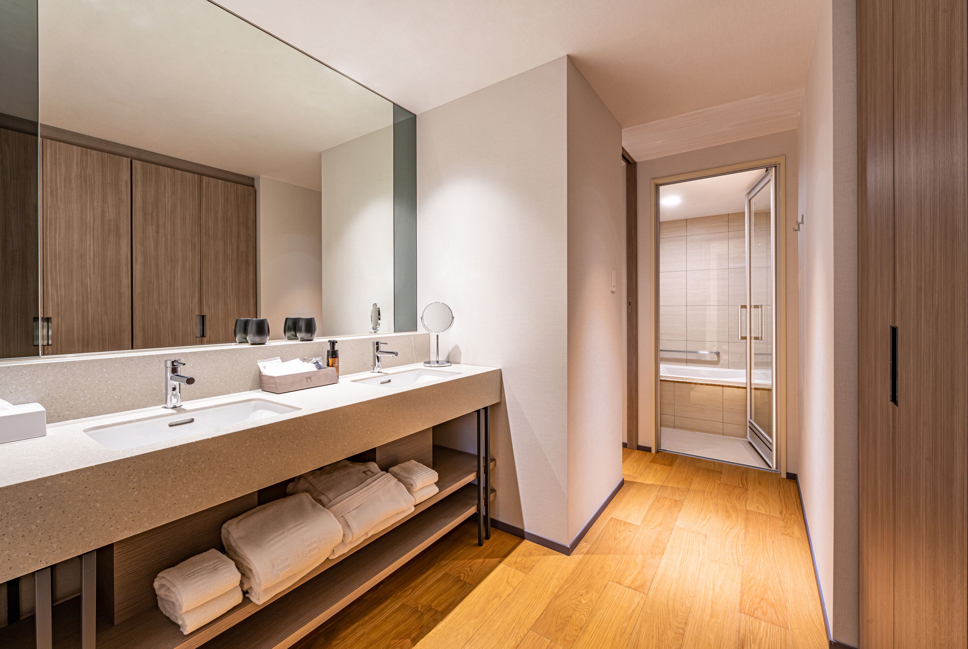 Een moderne badkamer met een grote spiegel, twee wasbakken, een douche en een houten vloer.