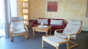 Uma sala de estar moderna com um sofá vermelho, duas poltronas brancas, uma mesa de centro de madeira e um quadro na parede.