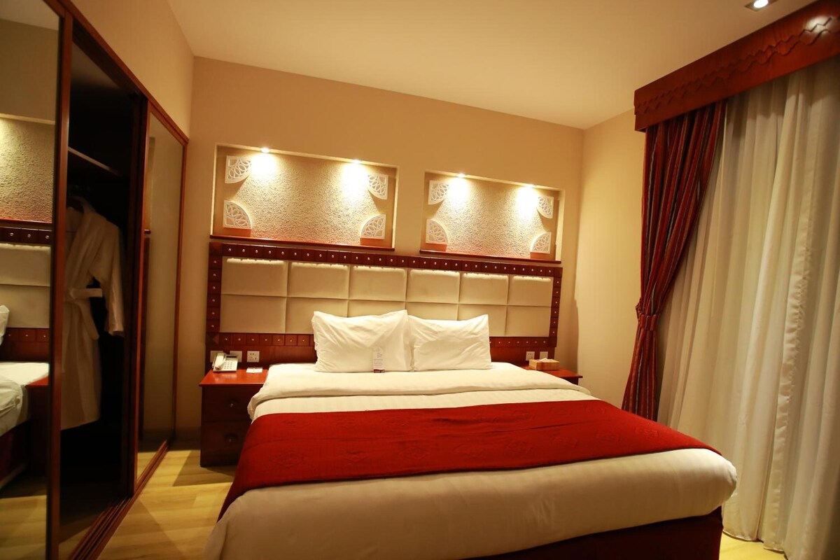 Habitación de hotel con una cama grande, cabecera de madera, mesita de noche con teléfono y armario.