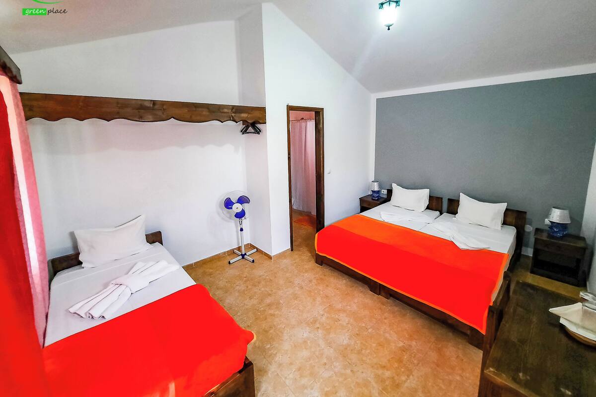 Quarto de hotel com duas camas, um ventilador, uma mesa de cabeceira e uma luminária no teto.