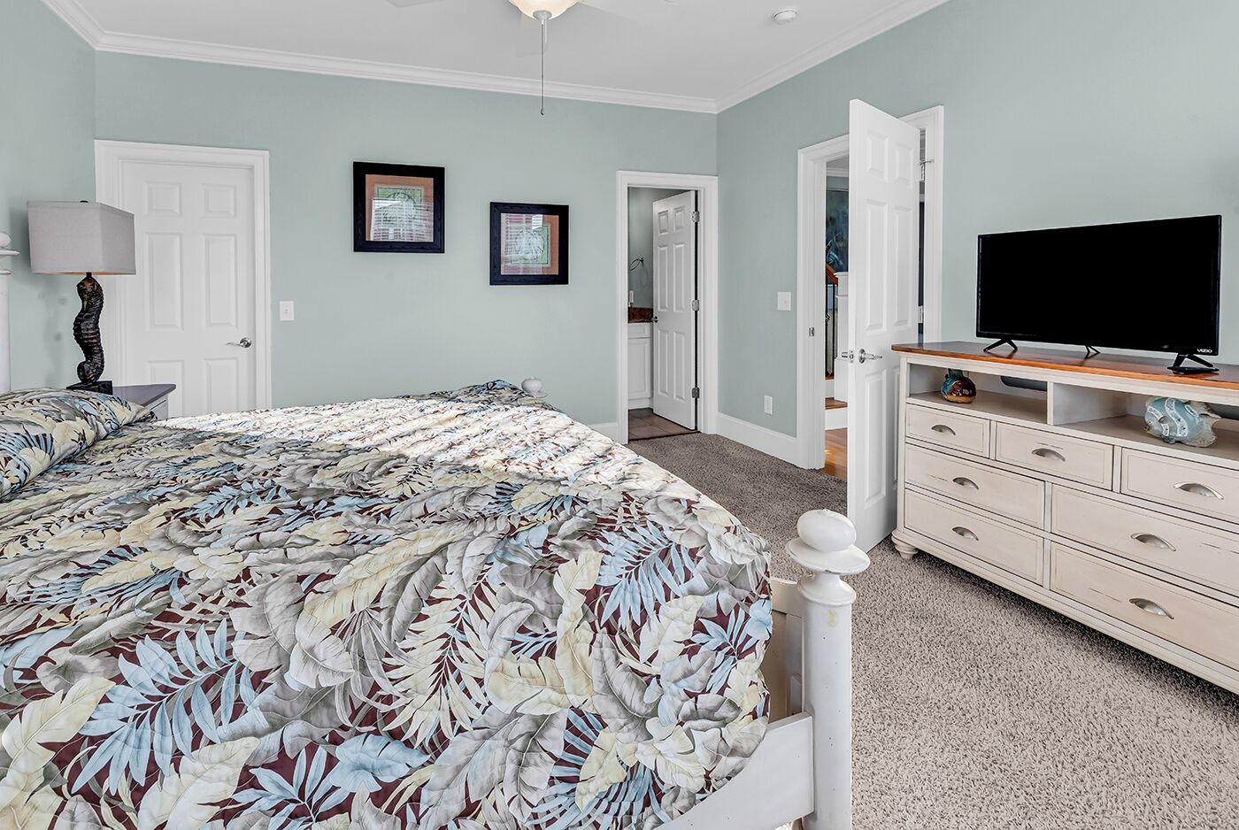 A bedroom with a bed, dresser, TV, and framed pictures on the wall.