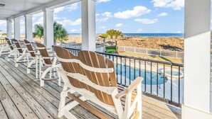 Une terrasse couverte avec des fauteuils Adirondack, une piscine et une vue sur la plage et l’océan.