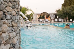 A pool area with a stone wall, lounge chairs, and a covered seating area. - Bellaria Residence (Giurdignano)