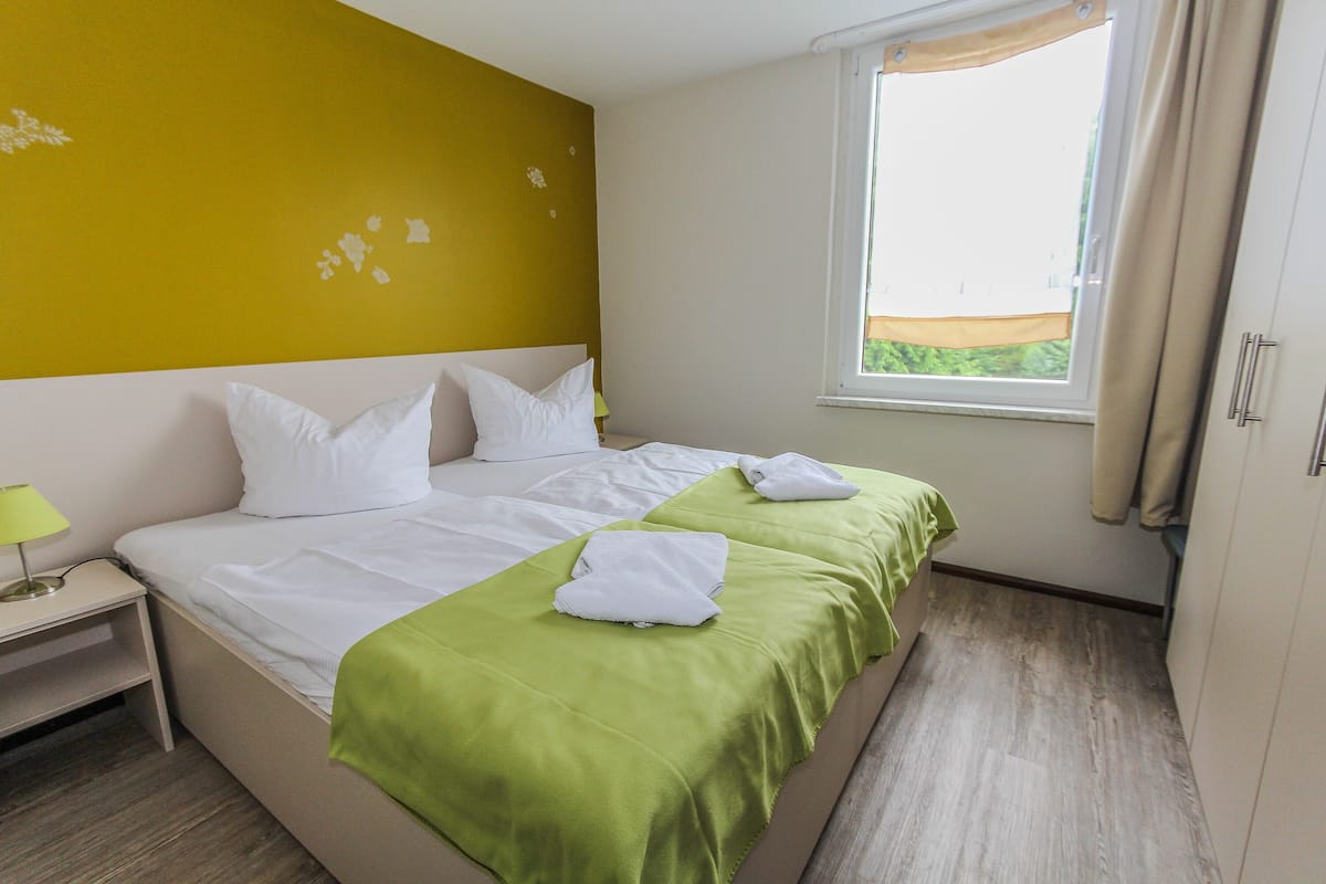 A hotel room with a bed, a nightstand, a window, and a wardrobe.