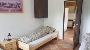 Una habitación pequeña y amoblada con cama, mesita de noche, armario y una puerta que da a la cocina.