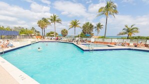 A rectangular swimming pool with clear blue water, surrounded by lounge chairs and palm trees.