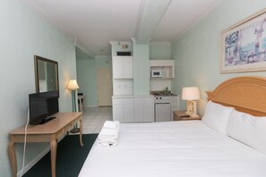 A hotel room with a bed, a desk with a television, a kitchenette, and a bathroom.
