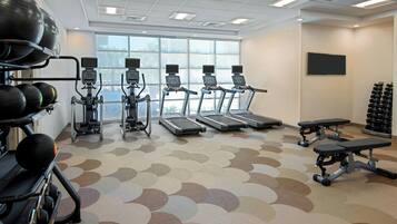 Un gimnasio con cintas de correr, elípticas y equipo de levantamiento de pesas.