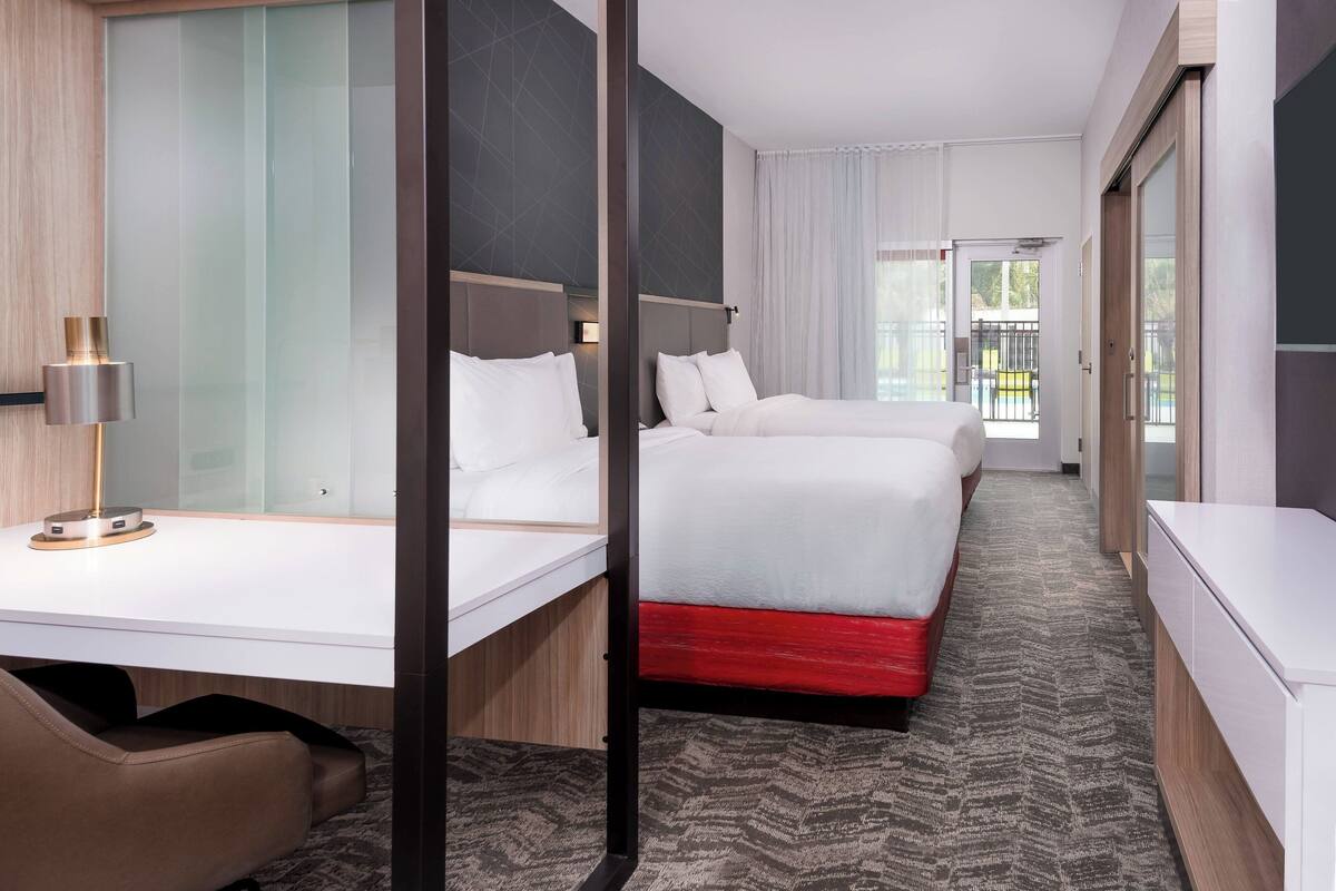 Een hotelkamer met twee bedden, een bureau, een stoel en uitzicht op het landschap.