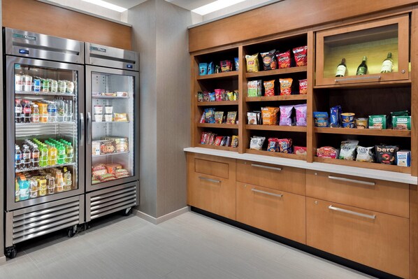 A kitchenette with two stainless steel refrigerators stocked with beverages and snacks, wooden cabinets with shelves holding various food items, and a countertop with a coffee machine. - SpringHill Suites by Marriott Lakeland (Lakeland)