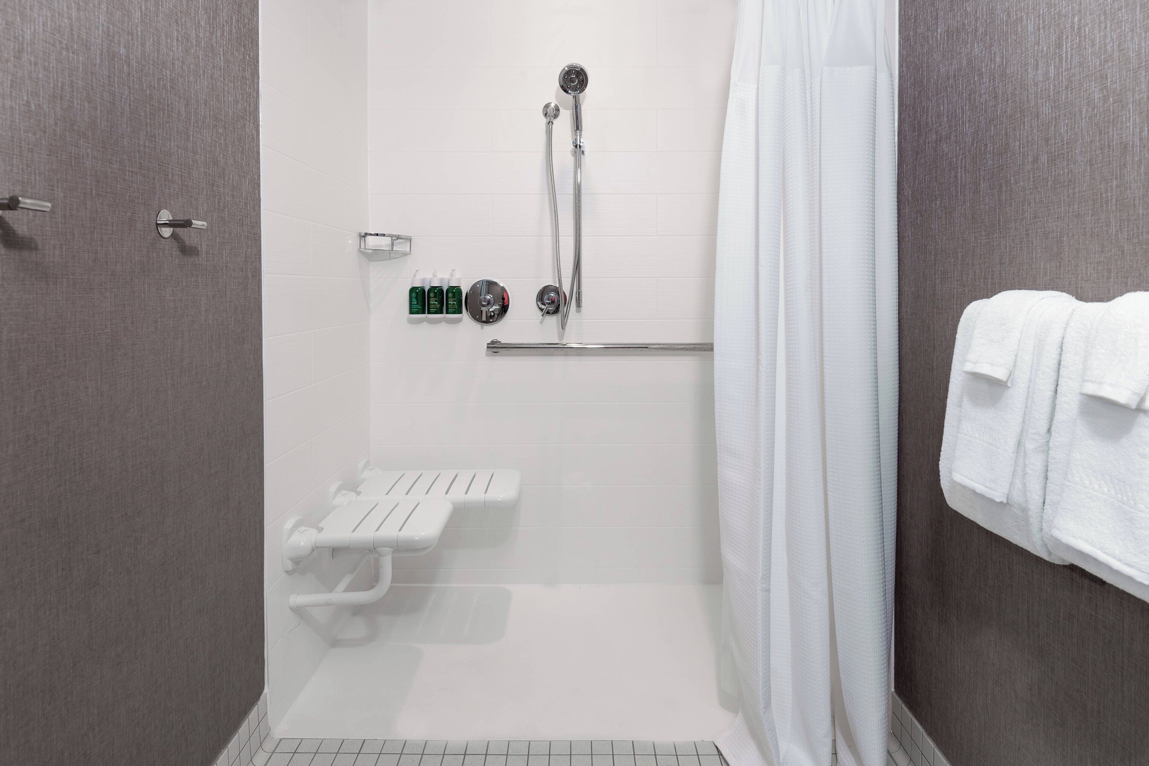 Un área de ducha moderna con ducha de mano, cabina de ducha de cristal y toallero blanco.