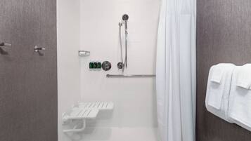 Un área de ducha moderna con ducha de mano, cabina de ducha de cristal y toallero blanco.
