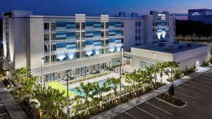 Ein modernes Hotel mit Poolbereich, Palmen und einem Parkplatz.