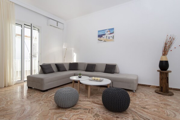A modern living room with a grey sectional sofa, two round ottomans, a small white coffee table, and a painting on the wall. - Downtown Apartment Paroikia (Paroikia Paros)