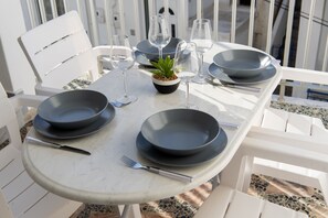 A table set with dark plates, wine glasses, and cutlery, surrounded by white chairs. - Downtown Apartment Paroikia (Paroikia Paros)
