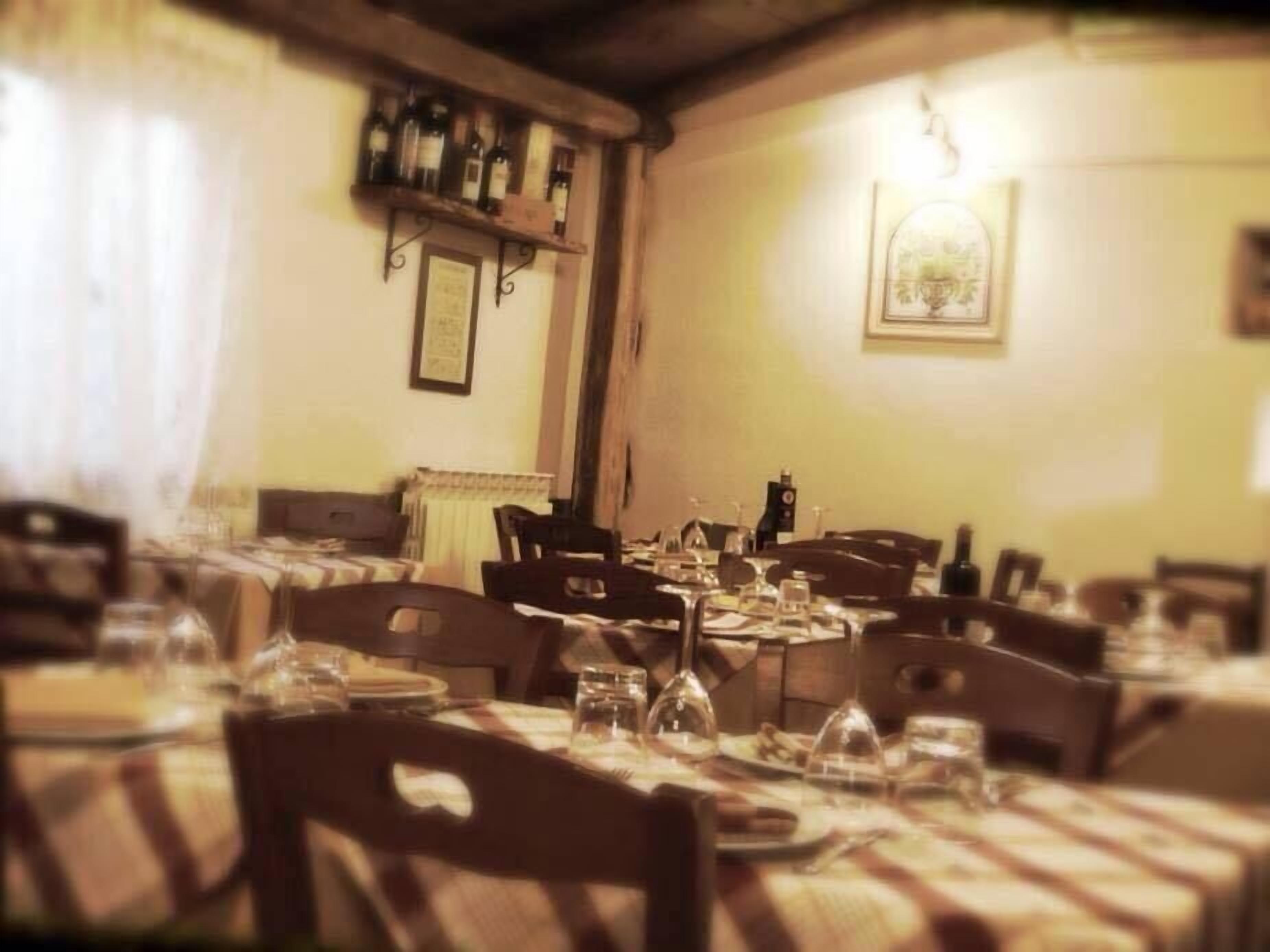 A dining area with multiple tables set for meals, wooden chairs, and a shelf with bottles.