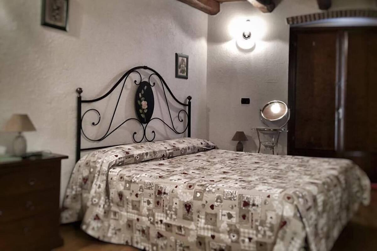A bedroom with a bed, a bedside table, a lamp, a mirror, and a wardrobe.