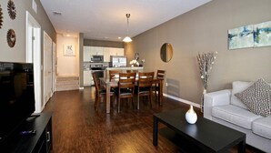 A modern living room with a dining area, kitchen in the background, and a sofa with decorative pillows. - Great townhouse in gated community, sleeps 6. 10 min to Disney! (Kissimmee)