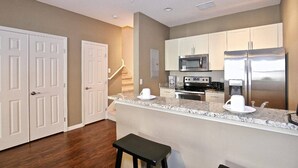A modern kitchen with white cabinetry, a stainless steel refrigerator, a microwave, and a stove. There is a small island with a coffee maker and a cup. - Great townhouse in gated community, sleeps 6. 10 min to Disney! (Kissimmee)
