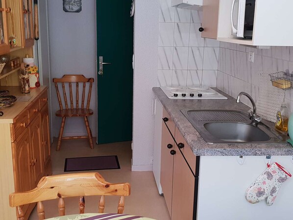 A compact kitchen with a stove, sink, and wooden chair.