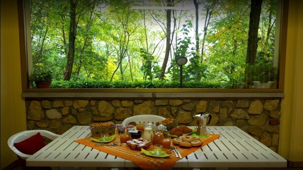 A table set with breakfast items, a view of a forest through a window, and a stone wall. - B&B Ca Di Me (Premariacco)