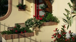 A house with a sloped roof, wooden beams, and brickwork. There are flower boxes with plants and flowers on the exterior walls. - B&B Ca Di Me (Premariacco)