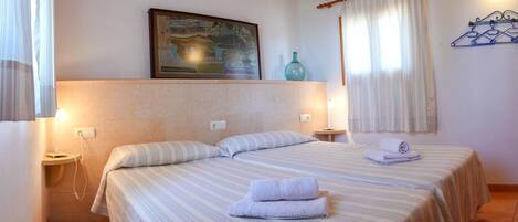 A hotel room with two beds, a painting on the wall, a window with curtains, and a wooden ceiling.