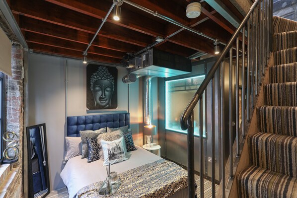 A modern bedroom with a large bed, a headboard, a nightstand, a lamp, and a window.
