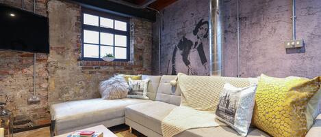 A cozy living room with a sectional sofa, a fireplace, and a rustic brick wall.