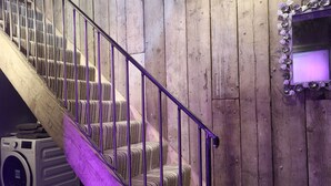 Un escalier en bois avec une rampe en métal, un lave-linge et un miroir avec un cadre violet.