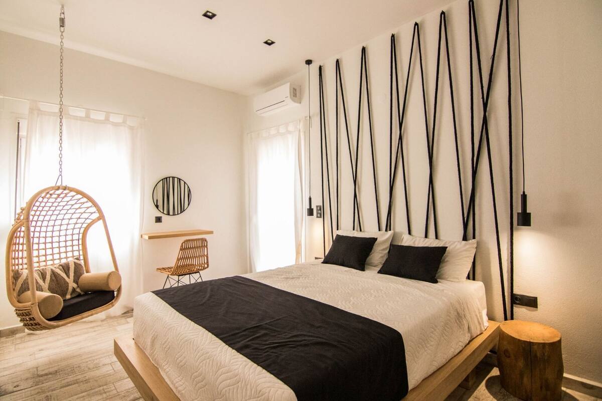 A modern bedroom with a hanging chair, a desk, and a bed with a black and white bedspread.