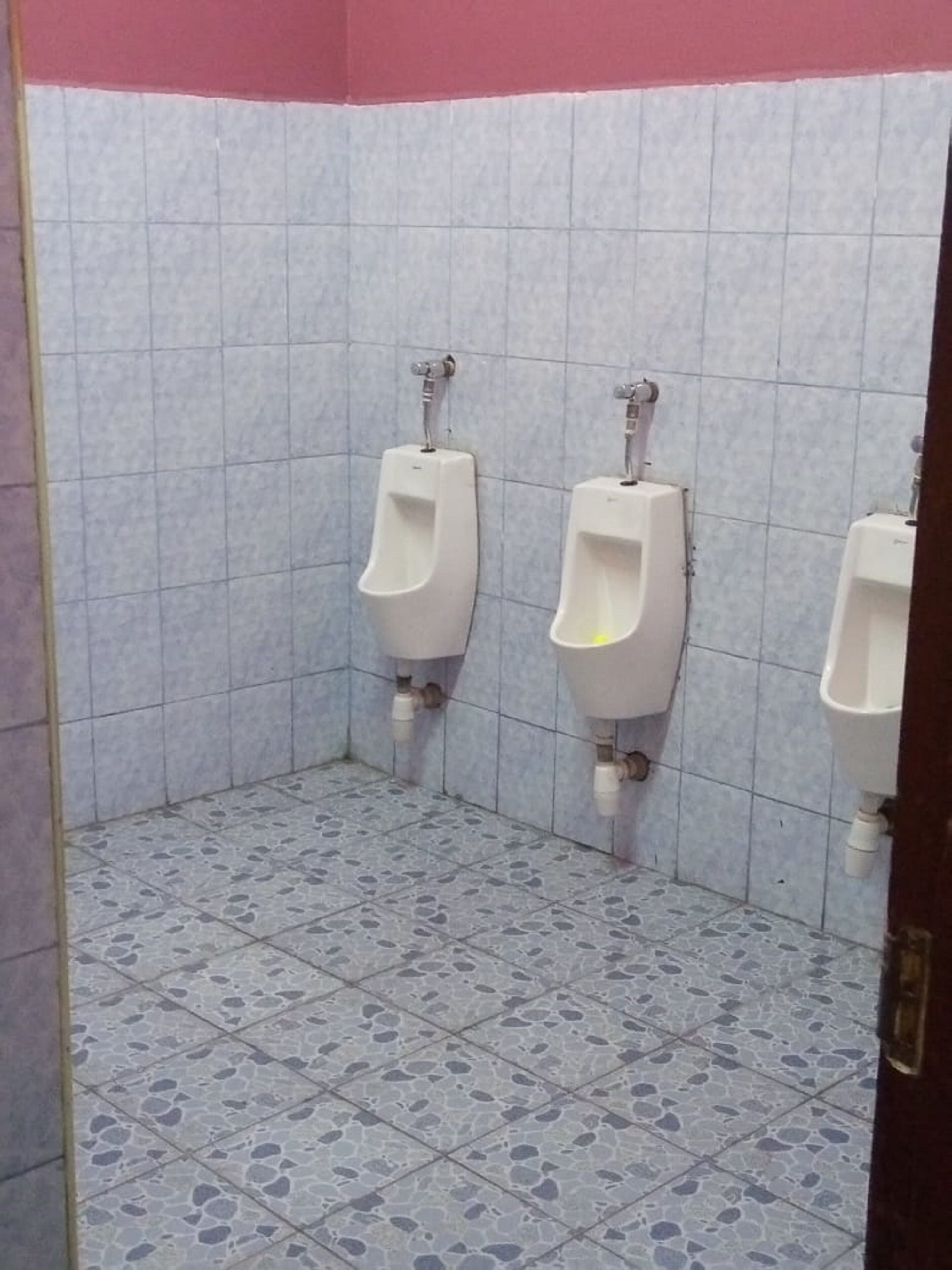 A public restroom with three urinals against a tiled wall, a tiled floor, and a pink ceiling.