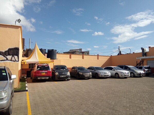 A parking lot with several cars parked in front of a building with a yellow tent and a mural of a bull. - Mayors Resort Centre (Nairobi)