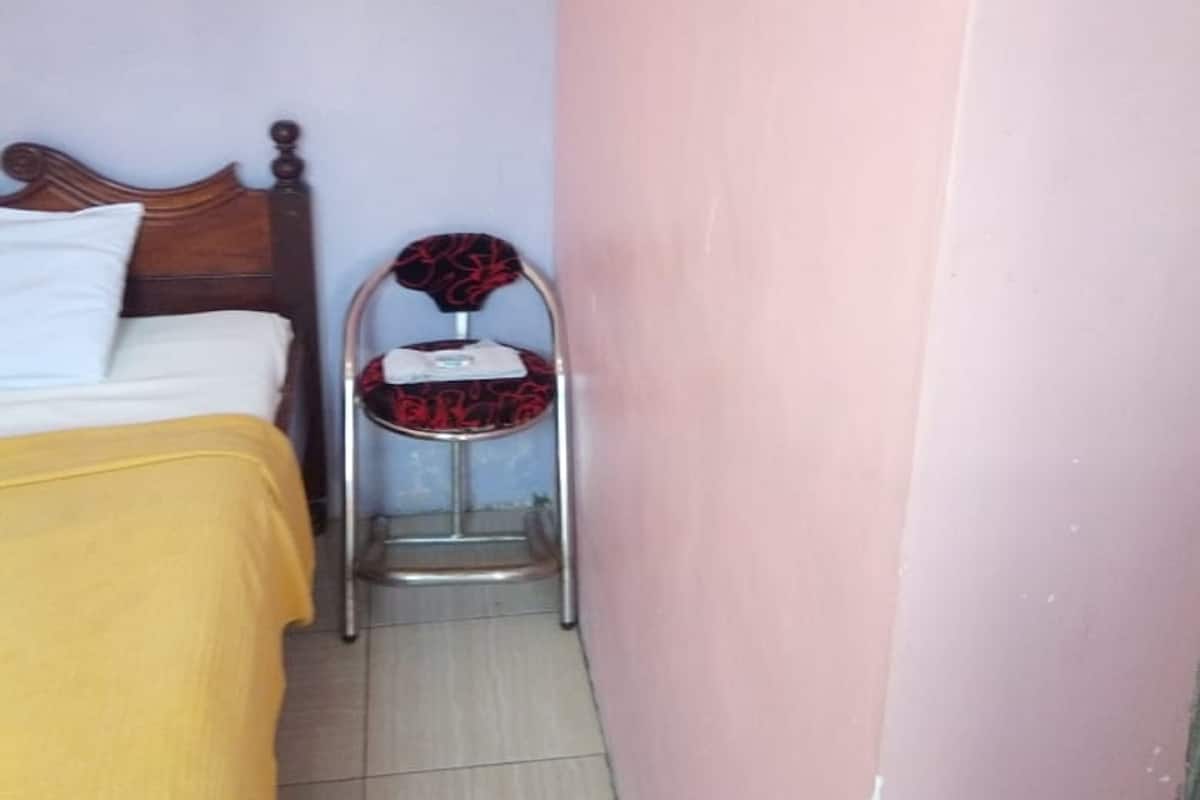 A small room with a bed, a chair, a small table, and a wall socket.