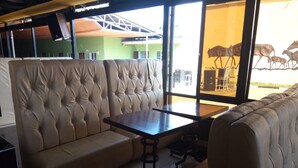 A seating area with a cushioned bench and a table, large windows, and a view of outdoor furniture. - Mayors Resort Centre (Nairobi)