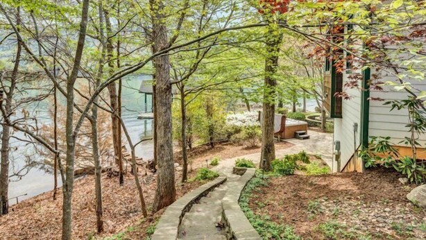 A serene lakeside property with a stone pathway leading to a wooden deck, surrounded by mature trees and a small gazebo. - Sandy Beach & Hot Tub! Iconic Mtn View! Come Visit "Sans Souci"! (Huddleston)