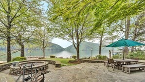 A stone patio with outdoor seating and a fire pit, overlooking a lake with mountains in the background. - Sandy Beach & Hot Tub! Iconic Mtn View! Come Visit "Sans Souci"! (Huddleston)