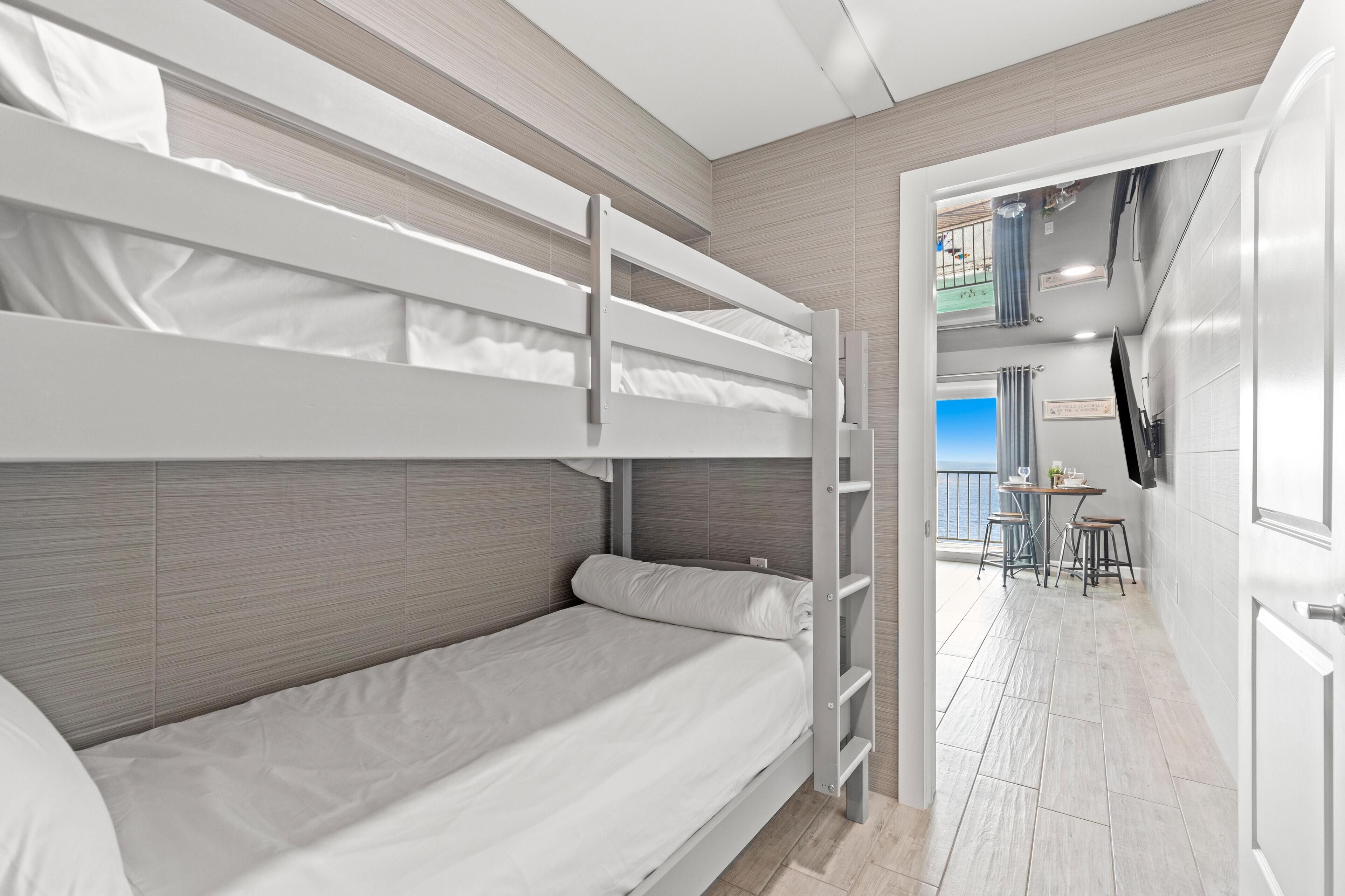 Habitación con literas, escritorio, silla, televisión montada en la pared y balcón con vistas.