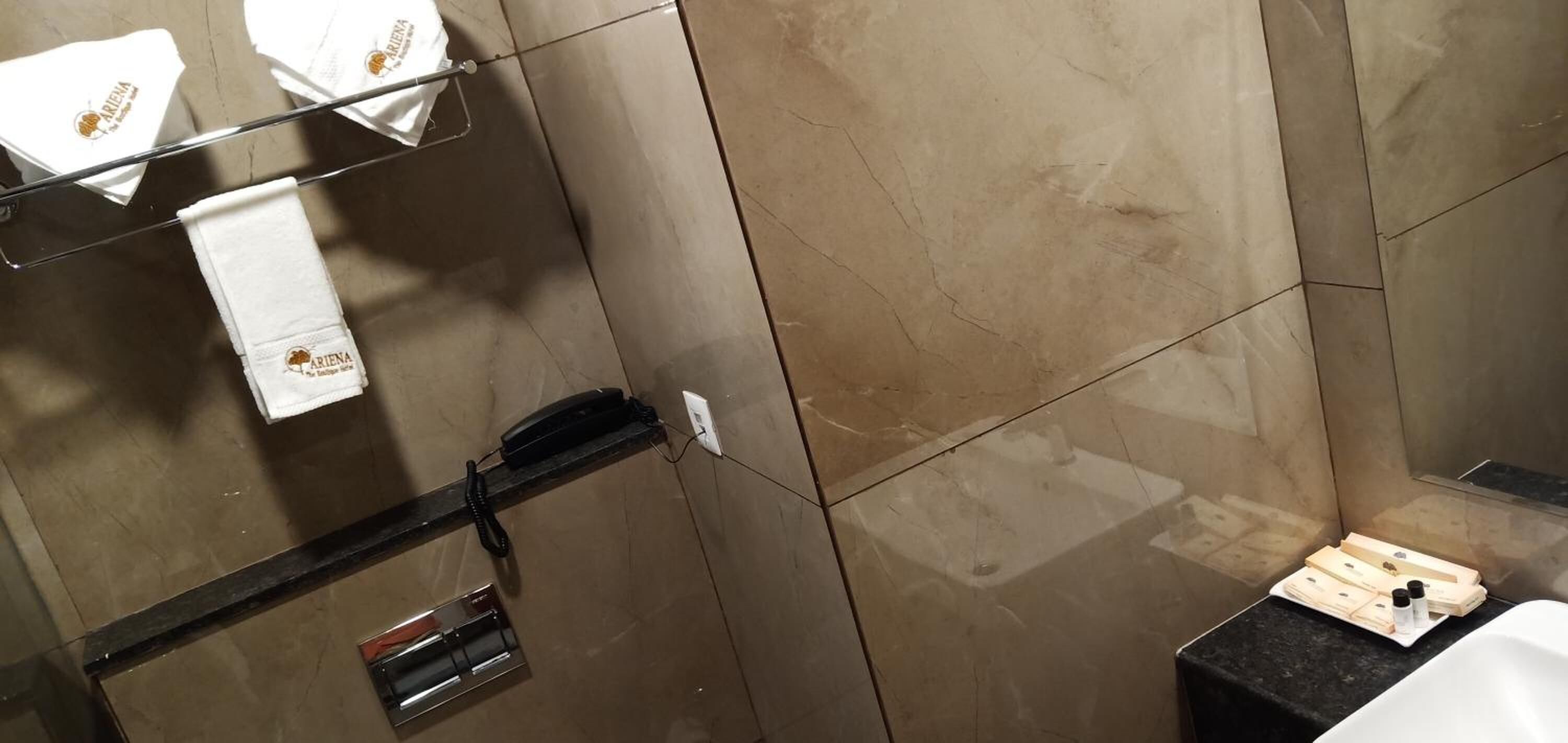 Un baño con piso de mármol, toallero negro, lavamanos blanco y una pequeña bandeja con artículos de tocador.