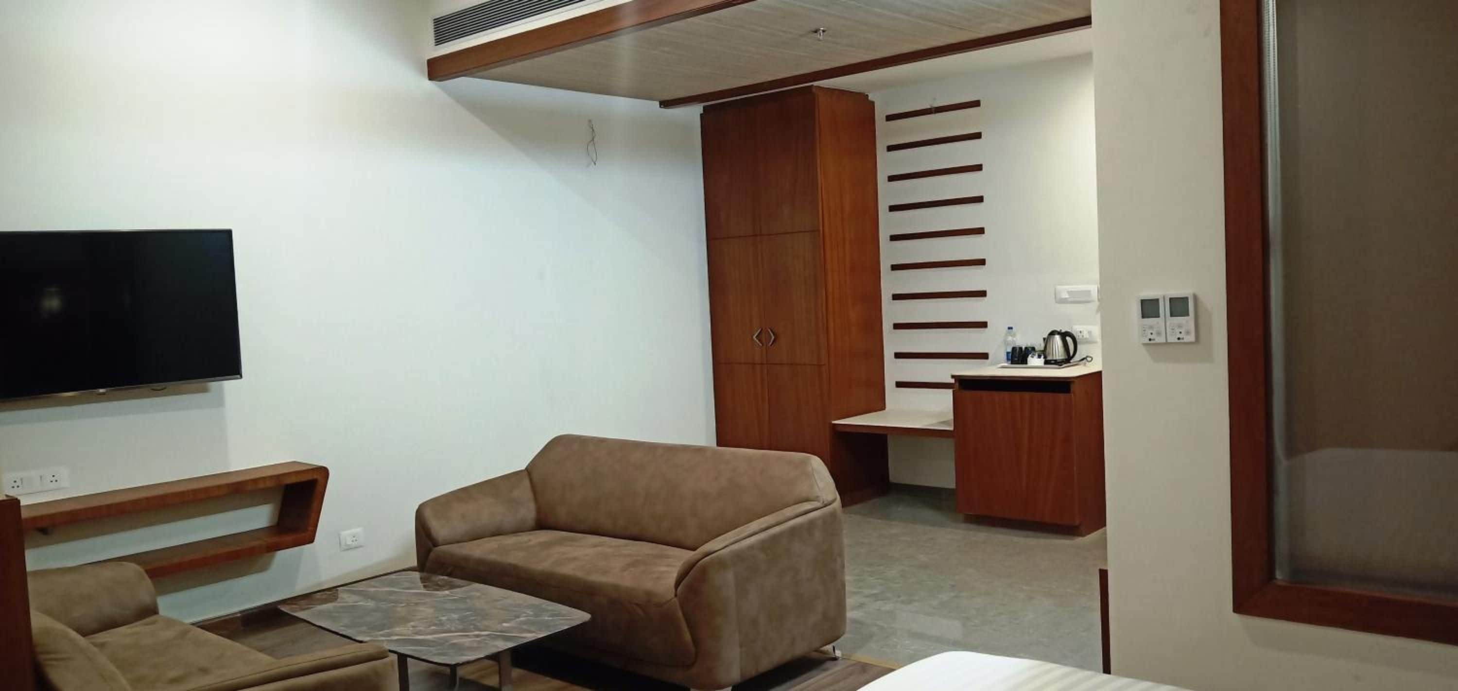 A modern living room with a sofa, a small table, a TV, and a kitchenette area with a sink and cabinets.