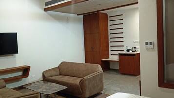 A modern living room with a sofa, a small table, a TV, and a kitchenette area with a sink and cabinets.