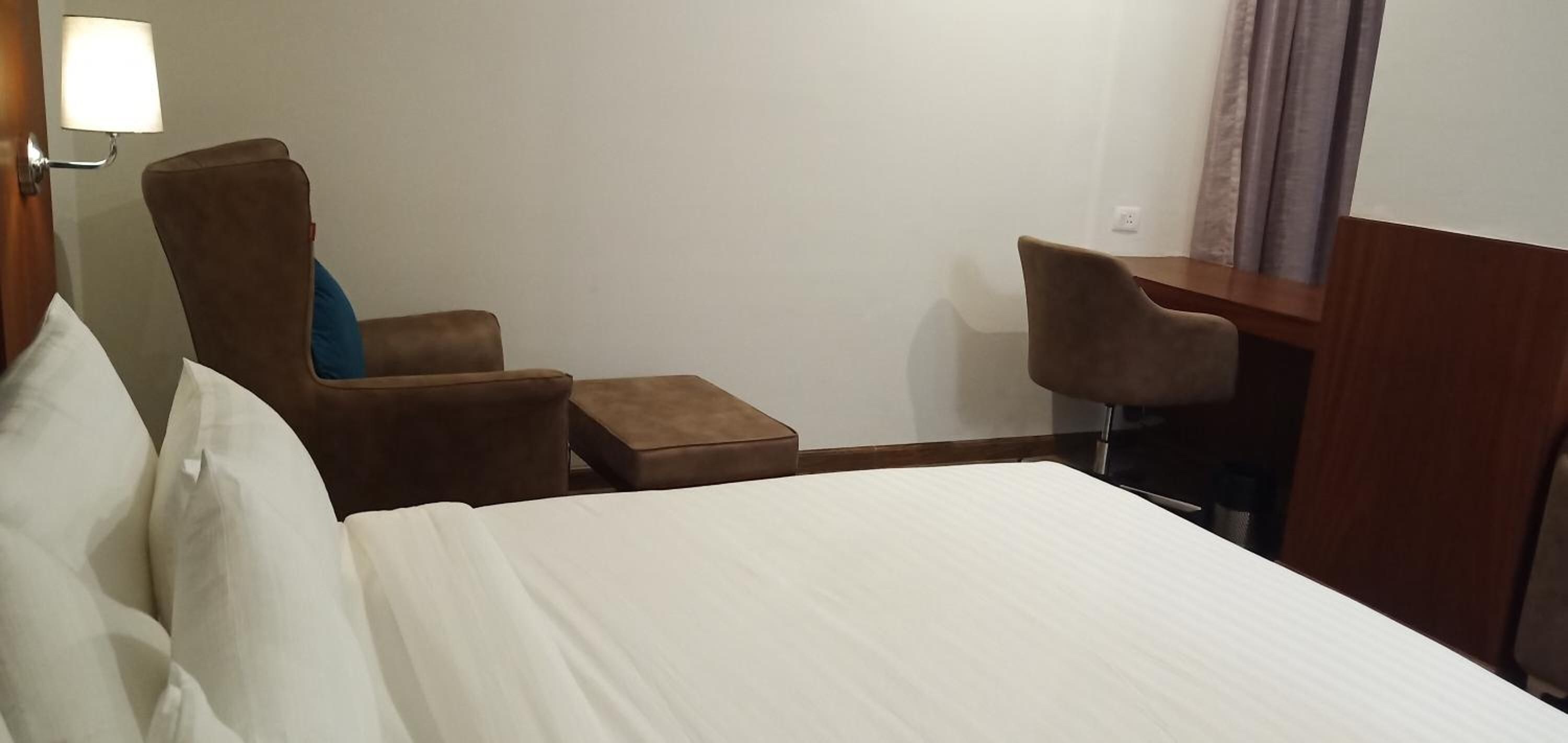 A hotel room with a bed, a chair, a small table, and a lamp.