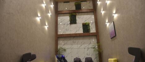 A modern waiting area with a tiered seating arrangement, a massage chair, and a wall with vertical gardens.