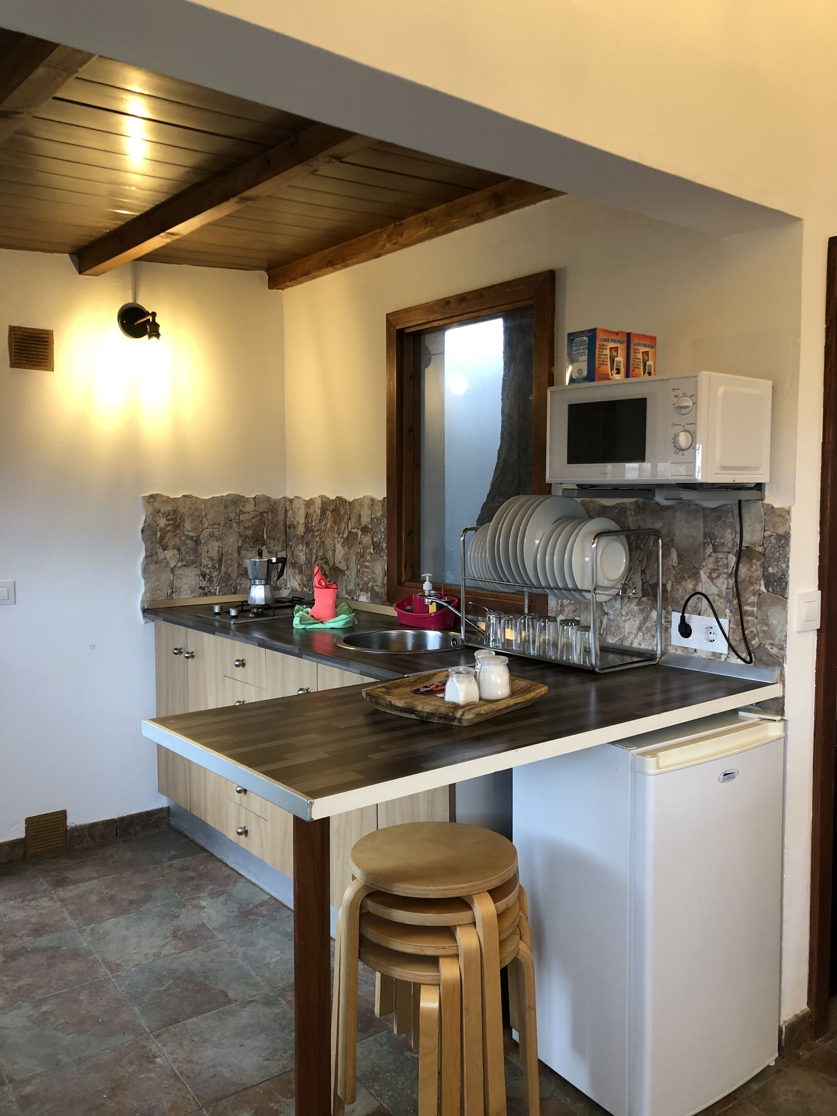 Een kleine keuken met een betegelde achterwand, een magnetron, een spoelbak en een kleine koelkast.