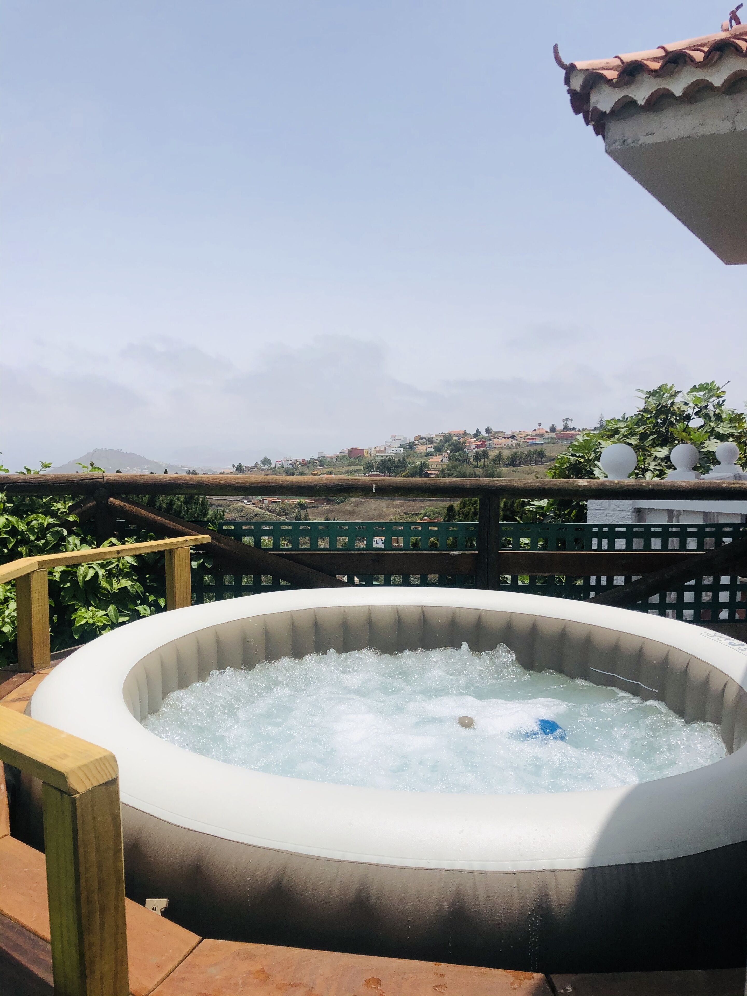 Un jacuzzi al aire libre con una terraza de madera y vistas a un pueblo en la ladera.